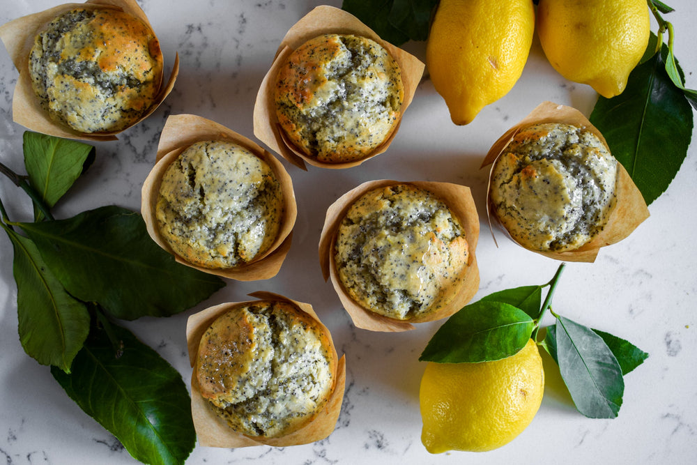 Freshly baked lemon and poppy seed muffins cooling on a rack with freshly picked lemons as decoration.