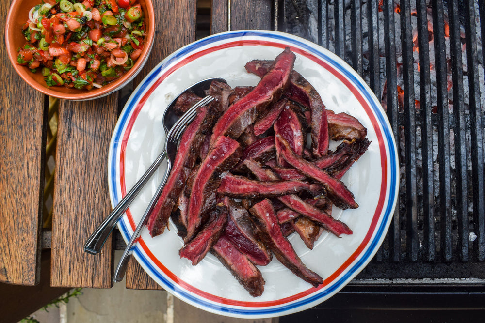 Medium-rare skirt steak sliced fresh off the grill placed in a bowl. Served alongside a side bowl of charred mixed pepper salsa.