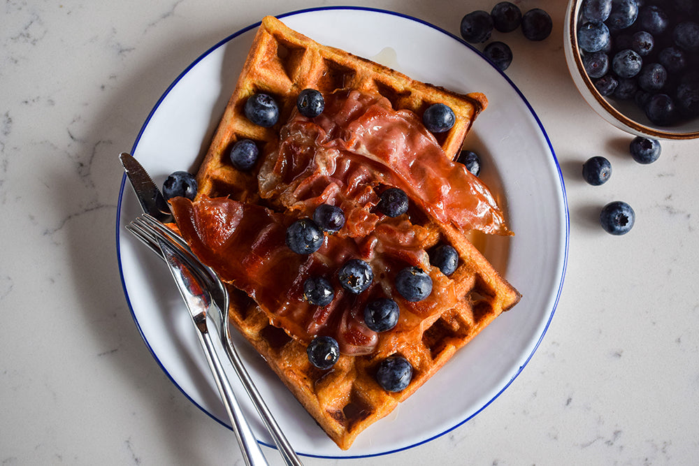 Sweet potato waffles stacked and topped with blueberries and crisp Parma ham.