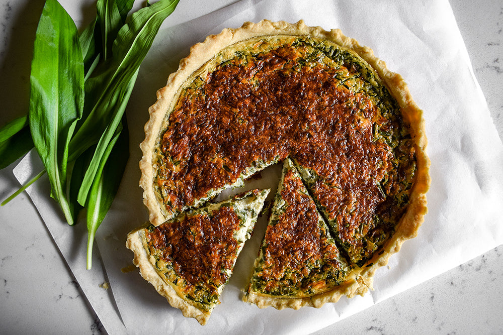A whole golden quiche sliced and presented with studded with wild garlic leaves on a plate.